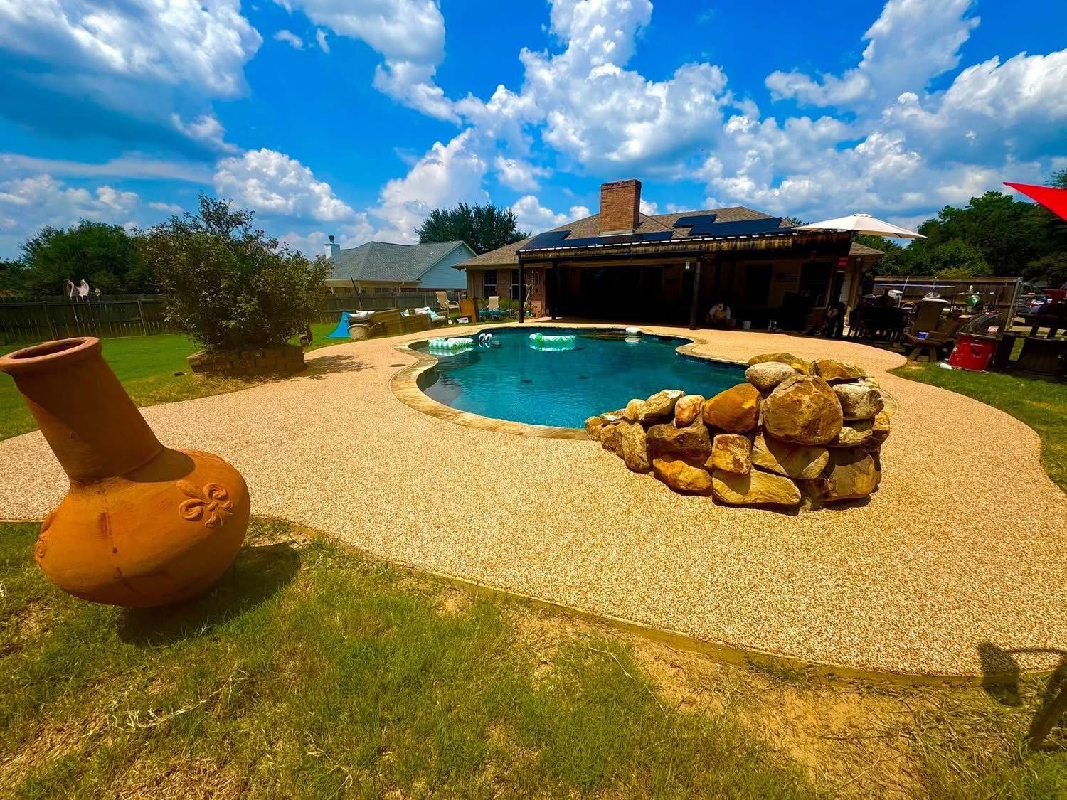 Backyard pool deck in tan speckled surfacing with a decorative stacked-stone accent