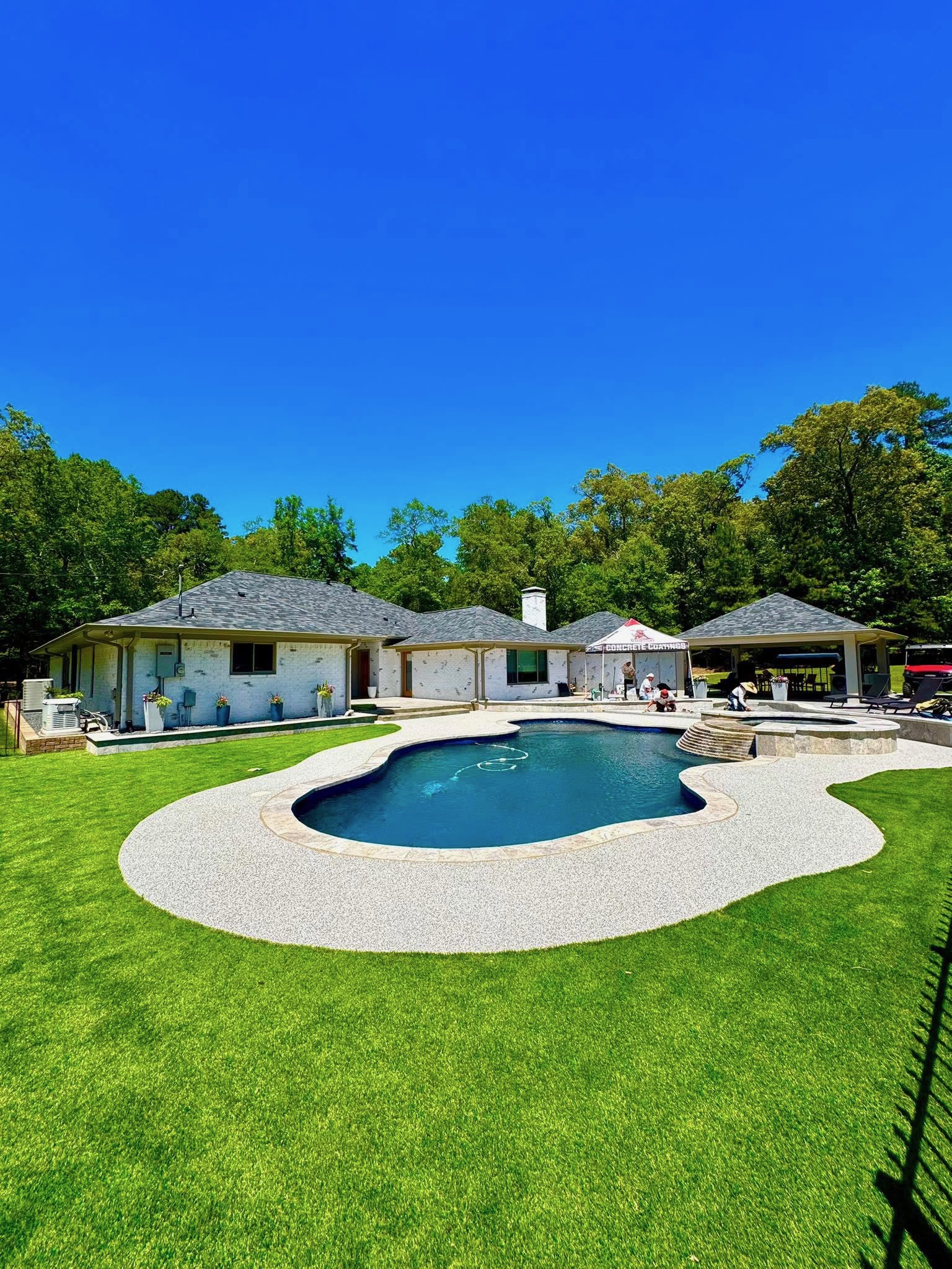 Kidney-shaped pool with light gray speckled deck surfacing bordered by artificial turf