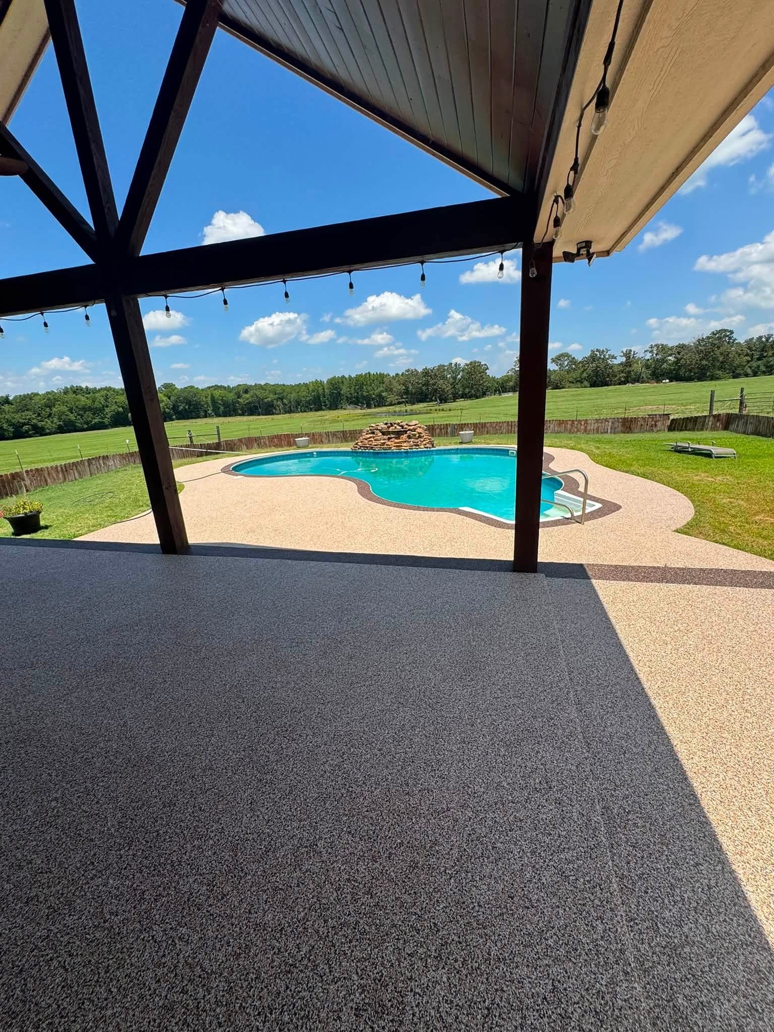 Covered patio view of a pool deck finished in two-tone tan and brown rubber surfacing