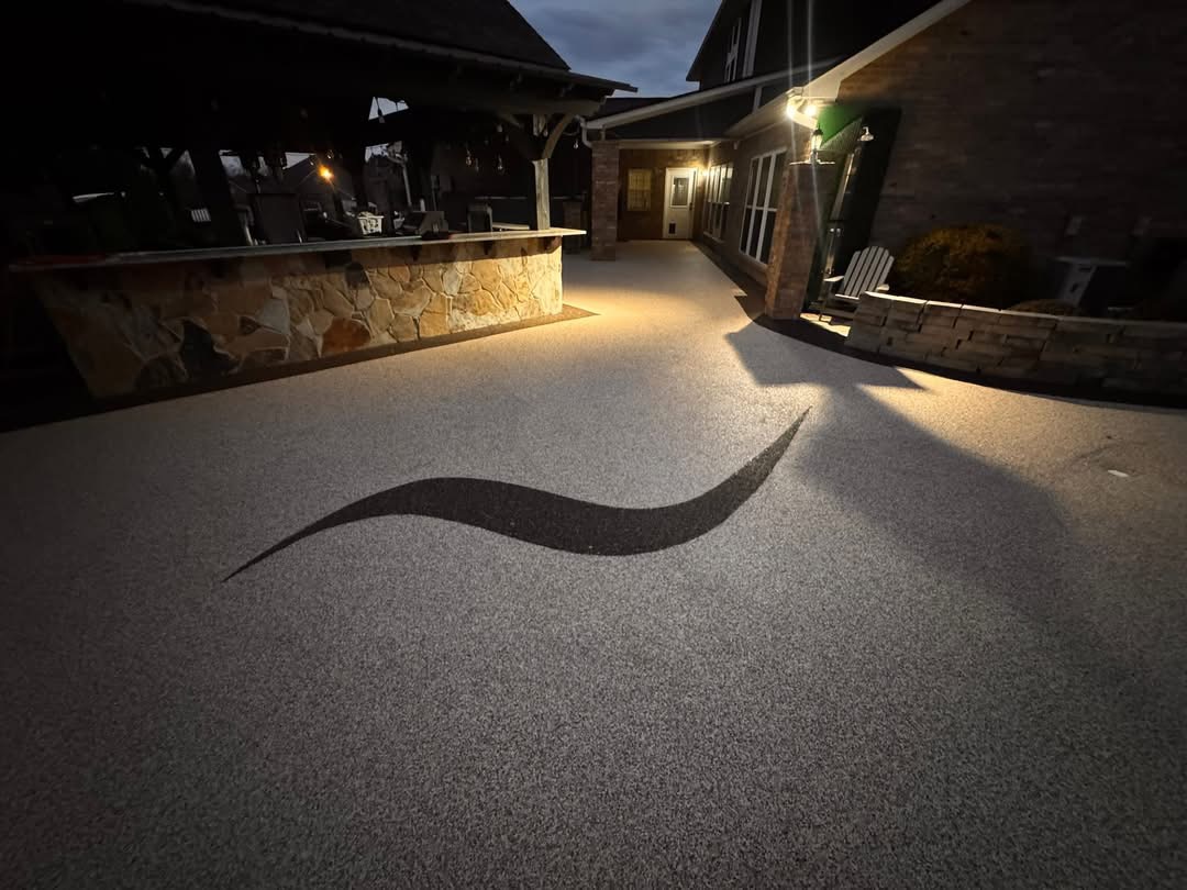 Evening view of a stone outdoor bar on gray speckled deck surfacing with a decorative wave inlay