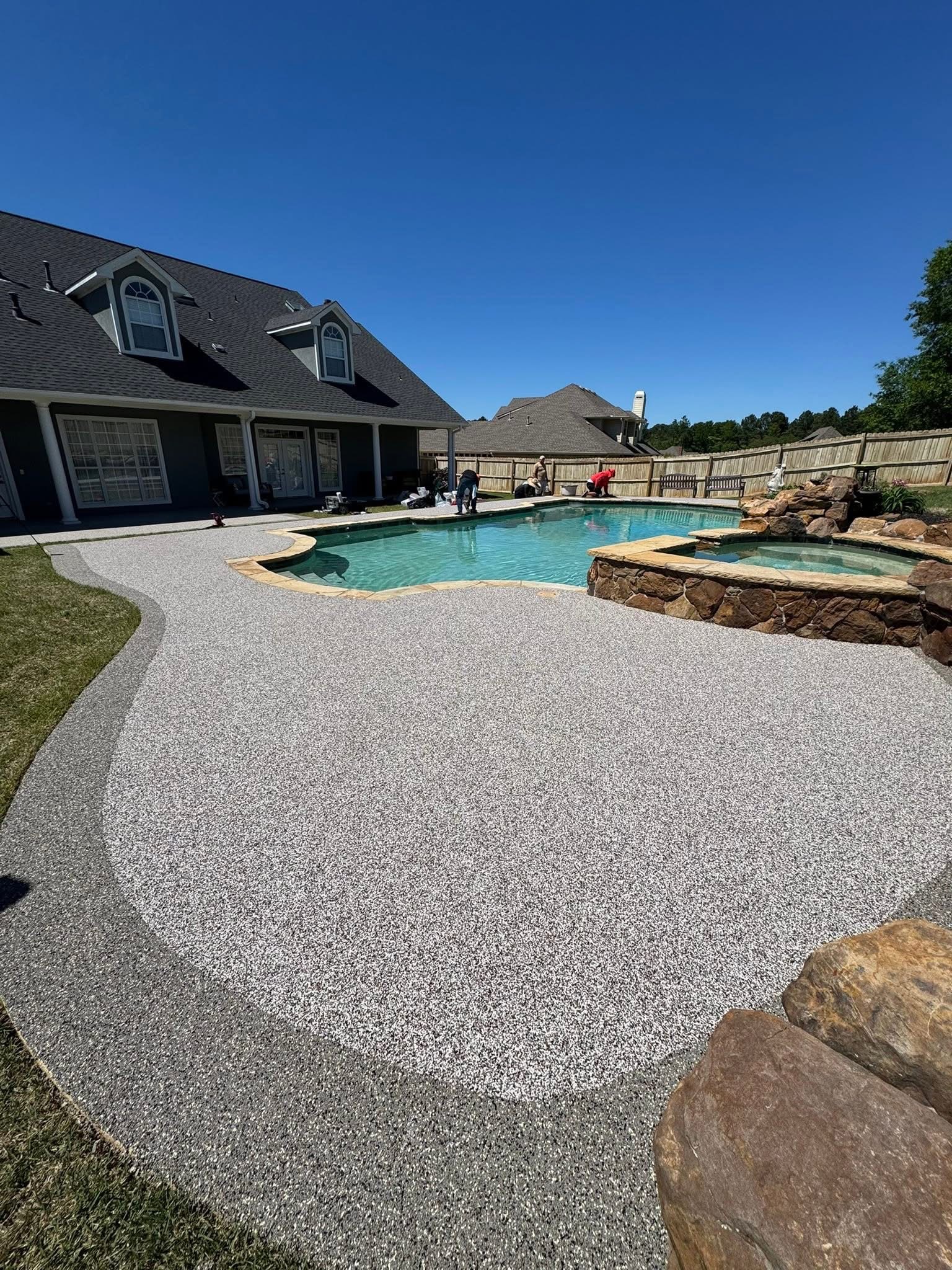 Crew installing gray and white speckled deck surfacing around a freeform pool and raised spa