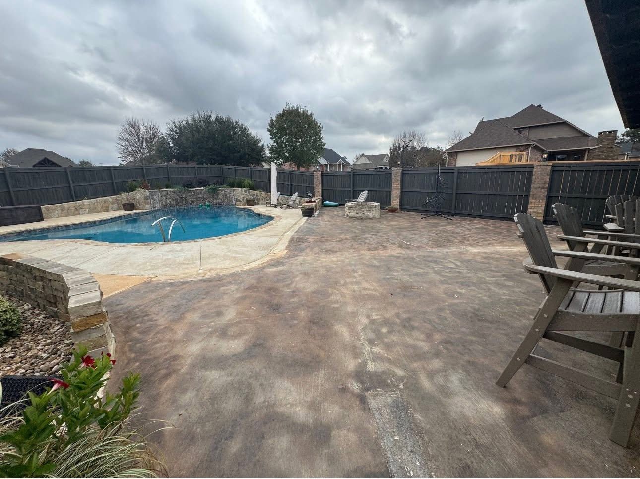Stained gray concrete pool patio with a stone accent wall before resurfacing