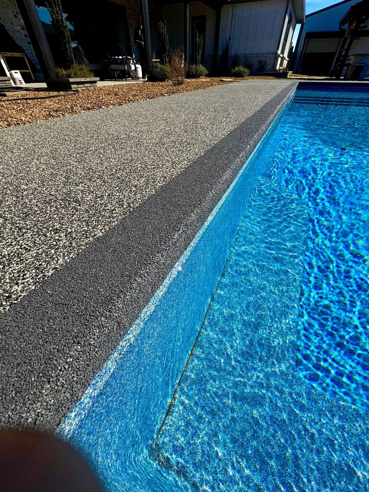 Close-up of dark coping band separating a speckled pool deck from the water