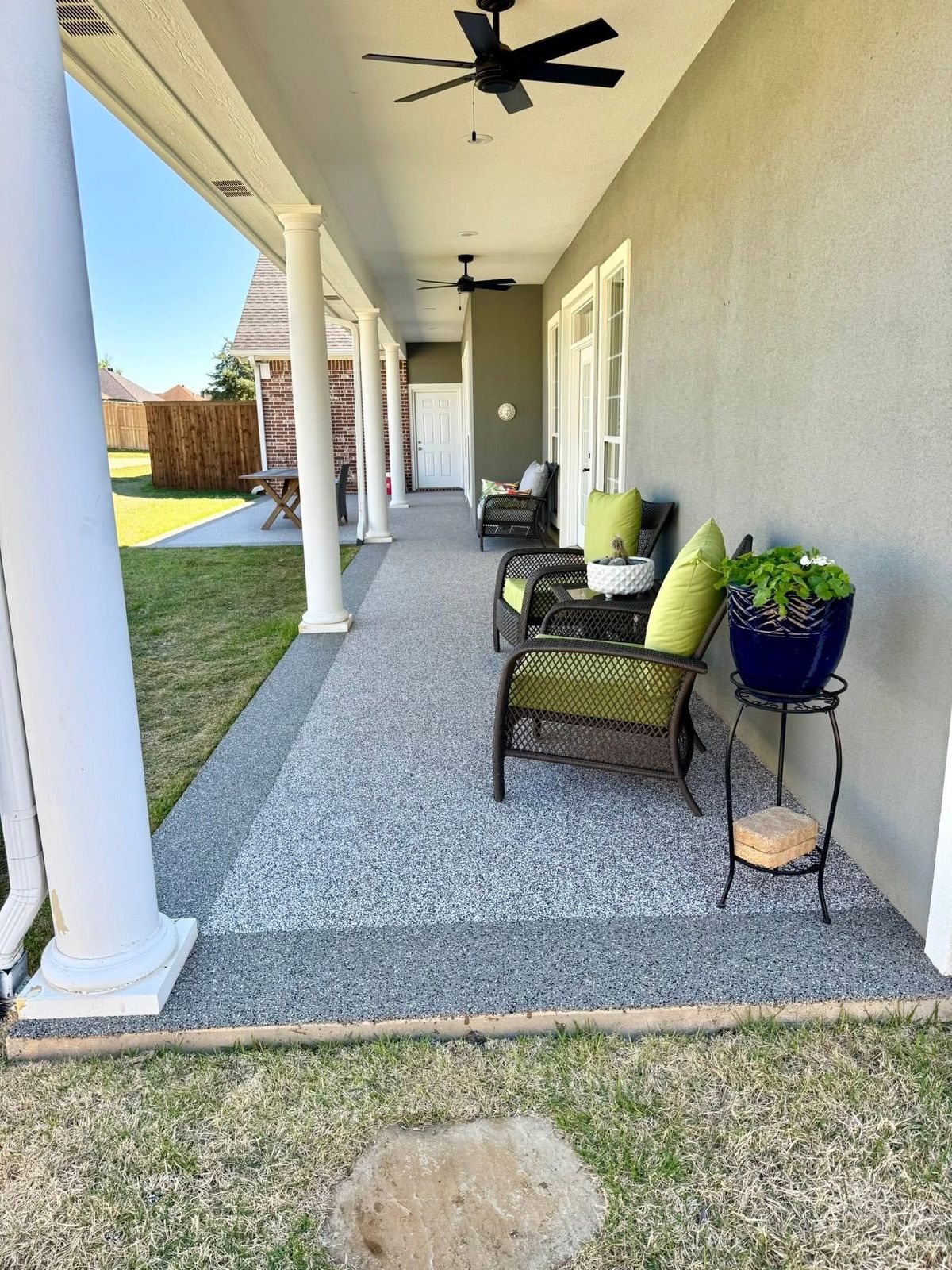 Covered porch with tan speckled flooring, outdoor seating, and potted plants