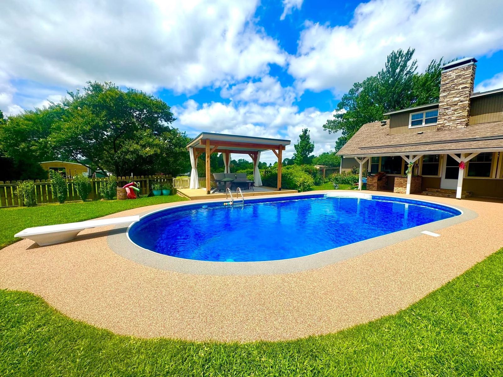 Freeform pool with tan speckled deck surfacing and covered patio in the background