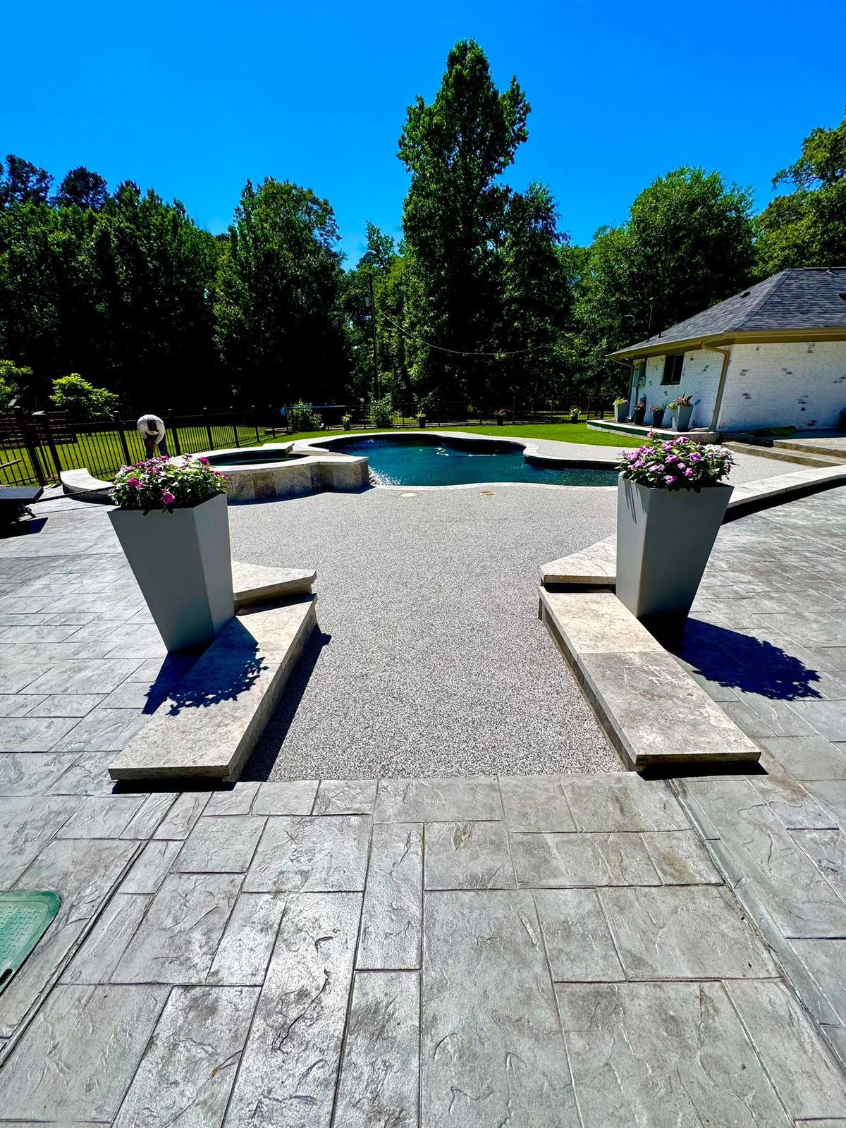 Stamped concrete courtyard leading to a freeform pool with a raised stacked-stone spa