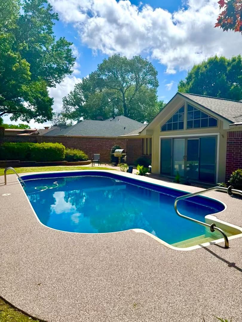 Vinyl liner pool with cream speckled deck surfacing in front of a brick home
