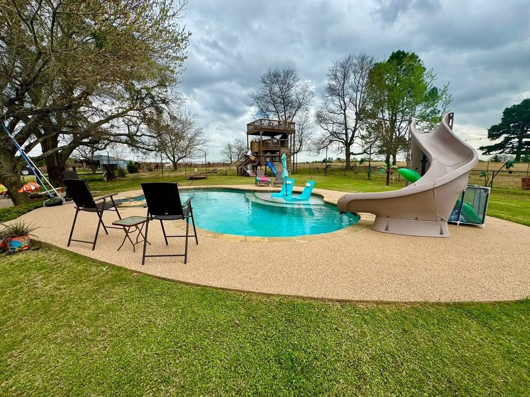 Backyard pool with a water slide and tan speckled deck surfacing