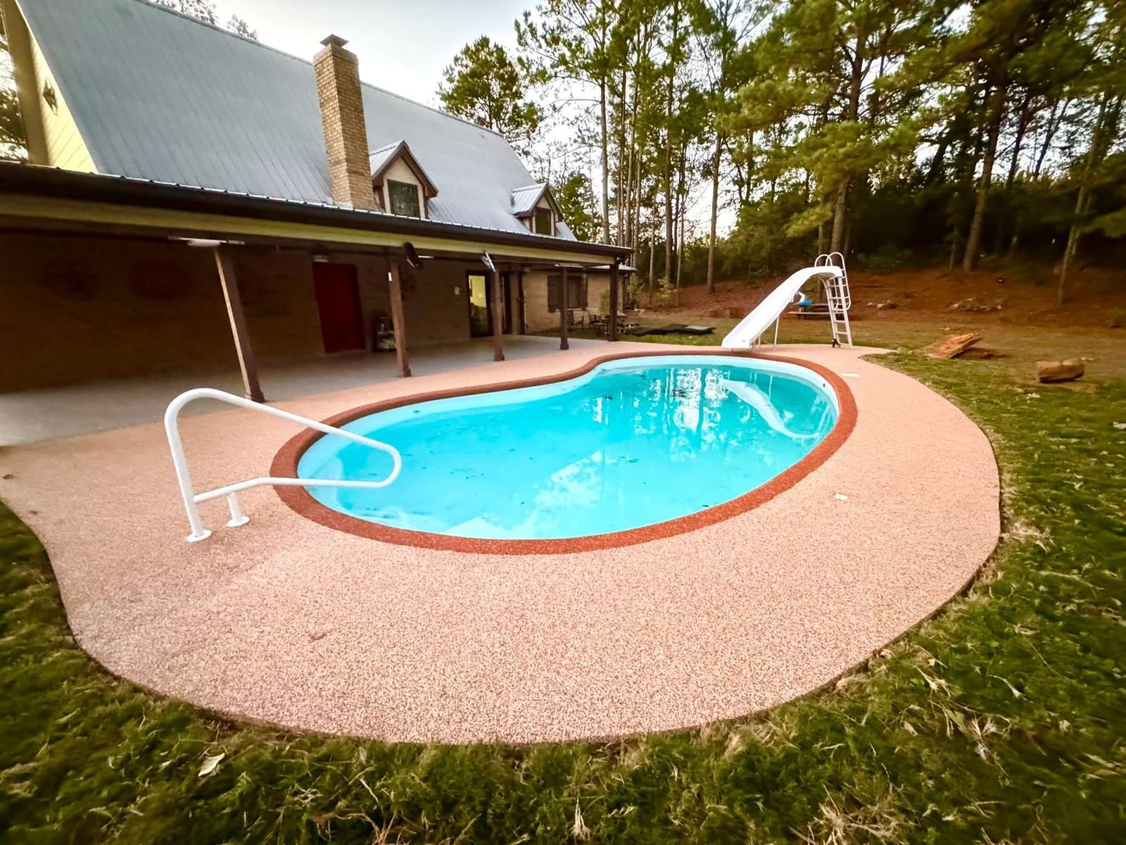 Finished kidney pool with red-bordered Pro-Flex deck surfacing in a wooded backyard