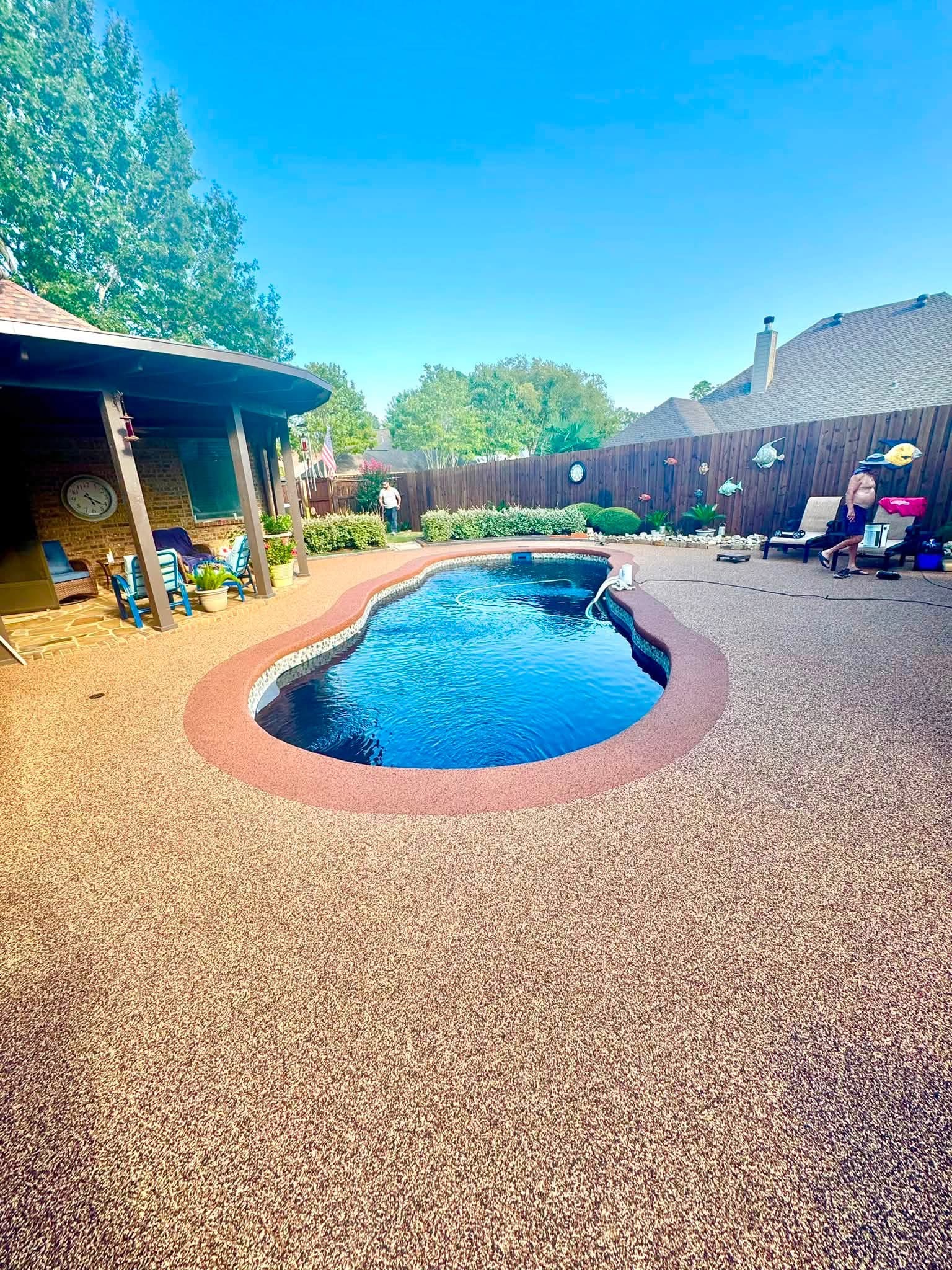 Kidney pool with tan speckled deck surfacing under a covered patio