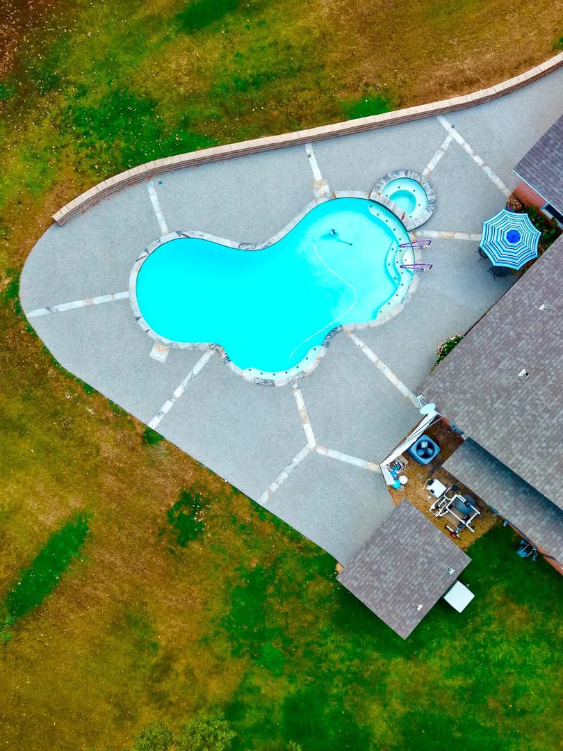 Aerial view of a freeform pool and spa with light gray speckled Pro-Flex deck surfacing