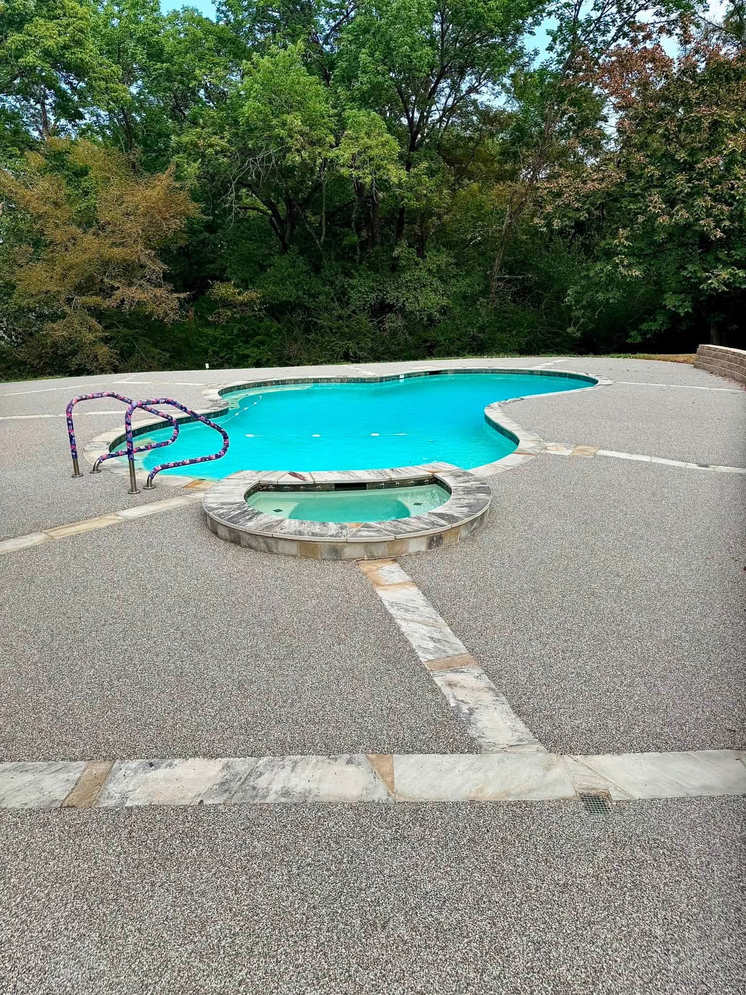 Freeform pool with raised spa and light gray speckled deck surfacing with stone accents