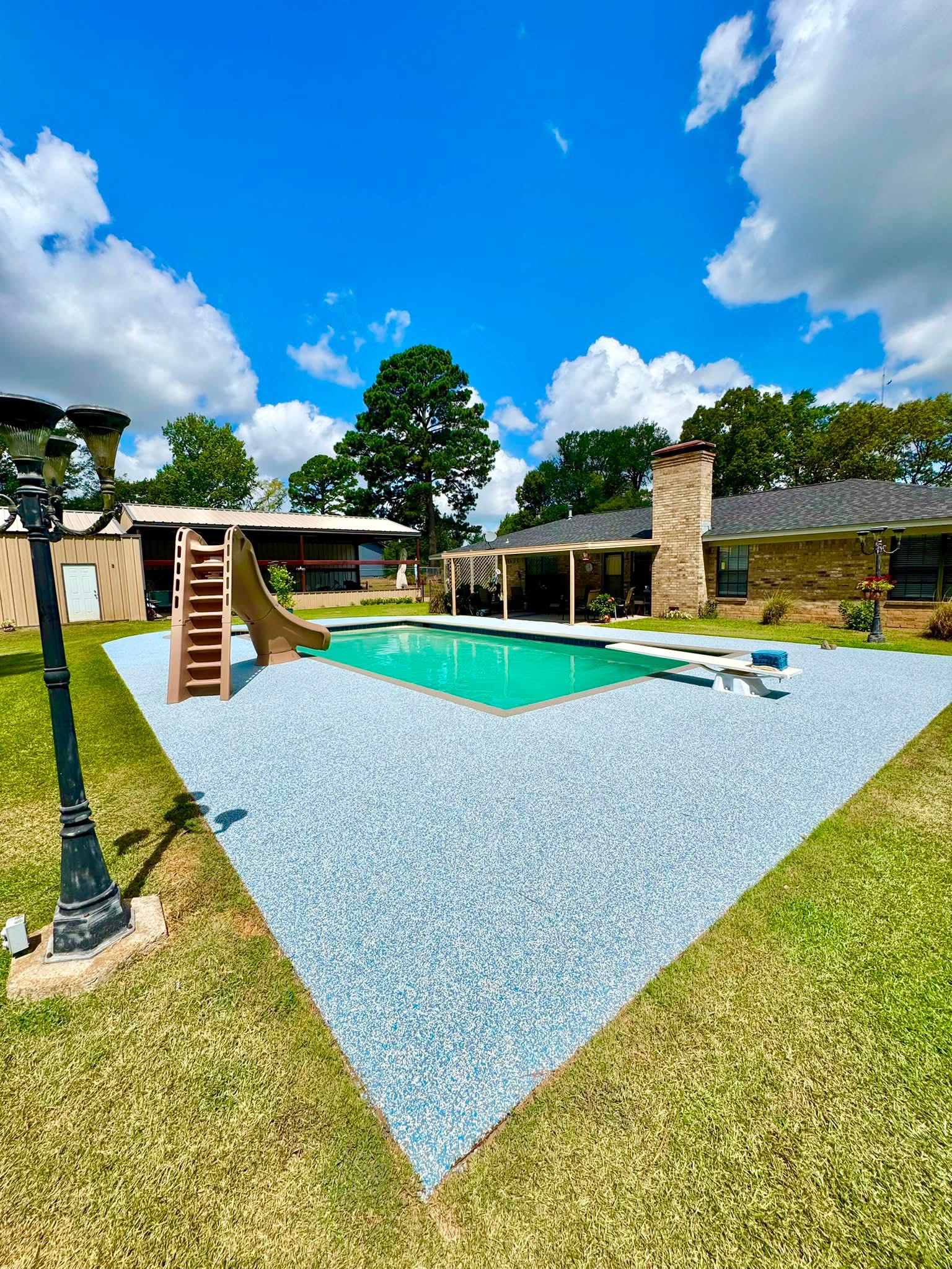 Rectangular pool with diving board and light blue speckled Pro-Flex deck surfacing