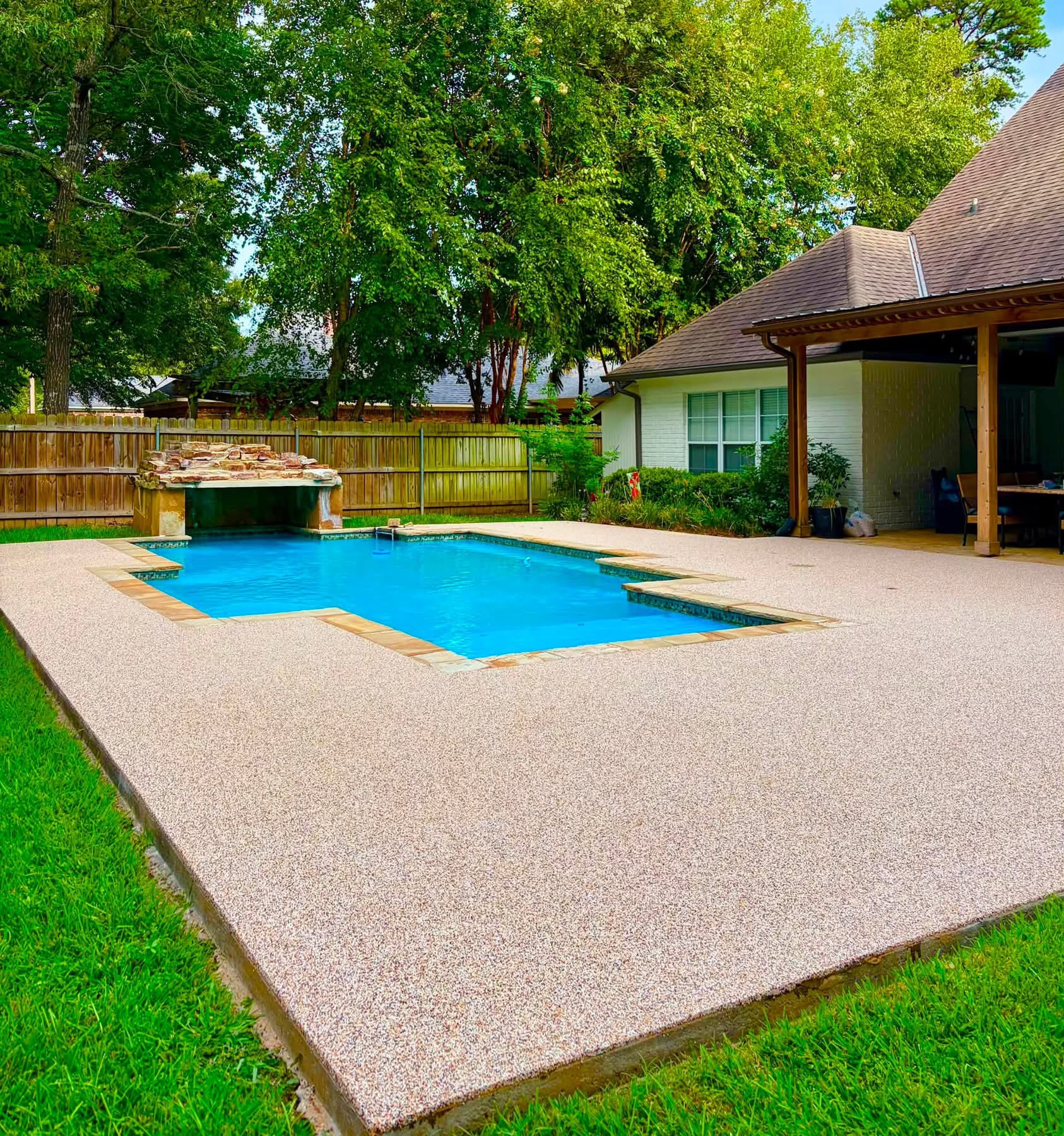 Rectangular pool with pink speckled deck surfacing and natural stone waterfall feature