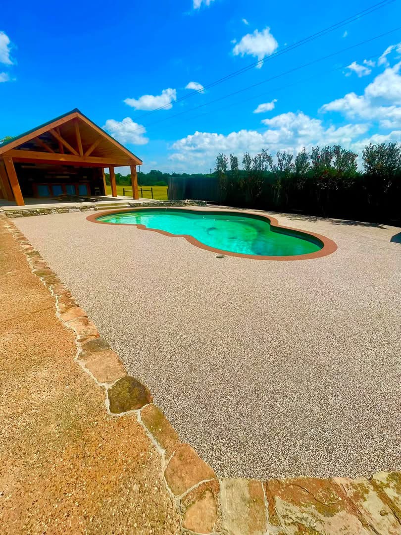 Freeform pool with gold speckled deck surfacing beside a timber pavilion