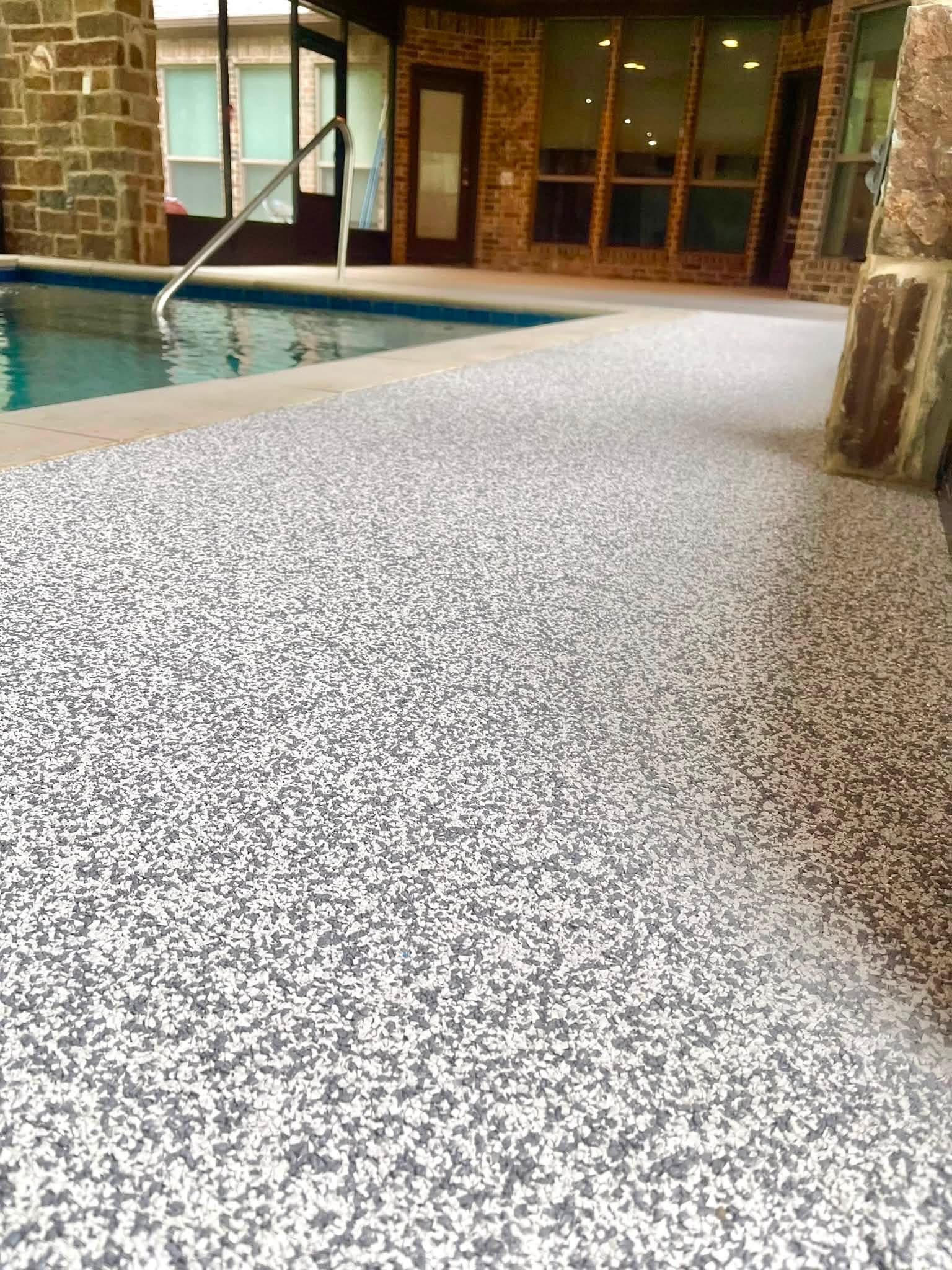 Screened-in pool deck finished in light gray speckled surfacing beside a brick sunroom