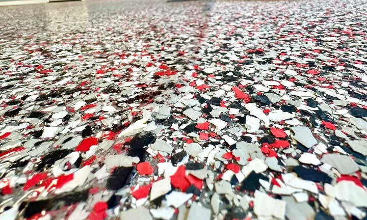 Close-up of red, black, and white decorative vinyl flake broadcast across a fresh coating