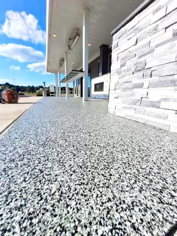Covered walkway finished with a tan speckled flake floor coating beside a home