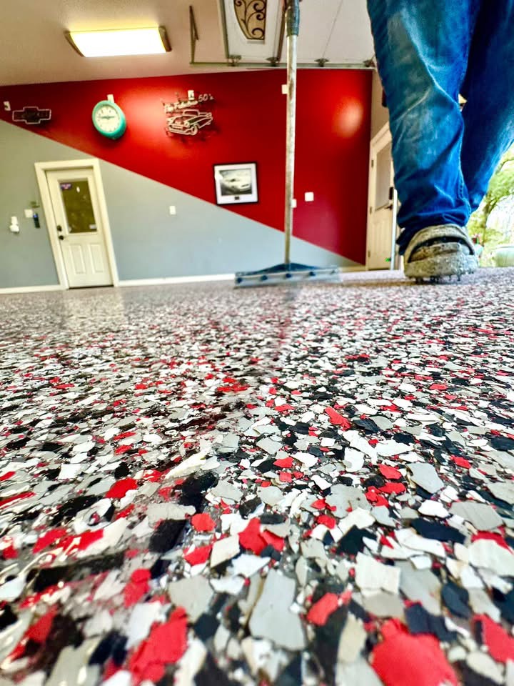Close-up of red, black, and white decorative flake being broadcast across a garage floor