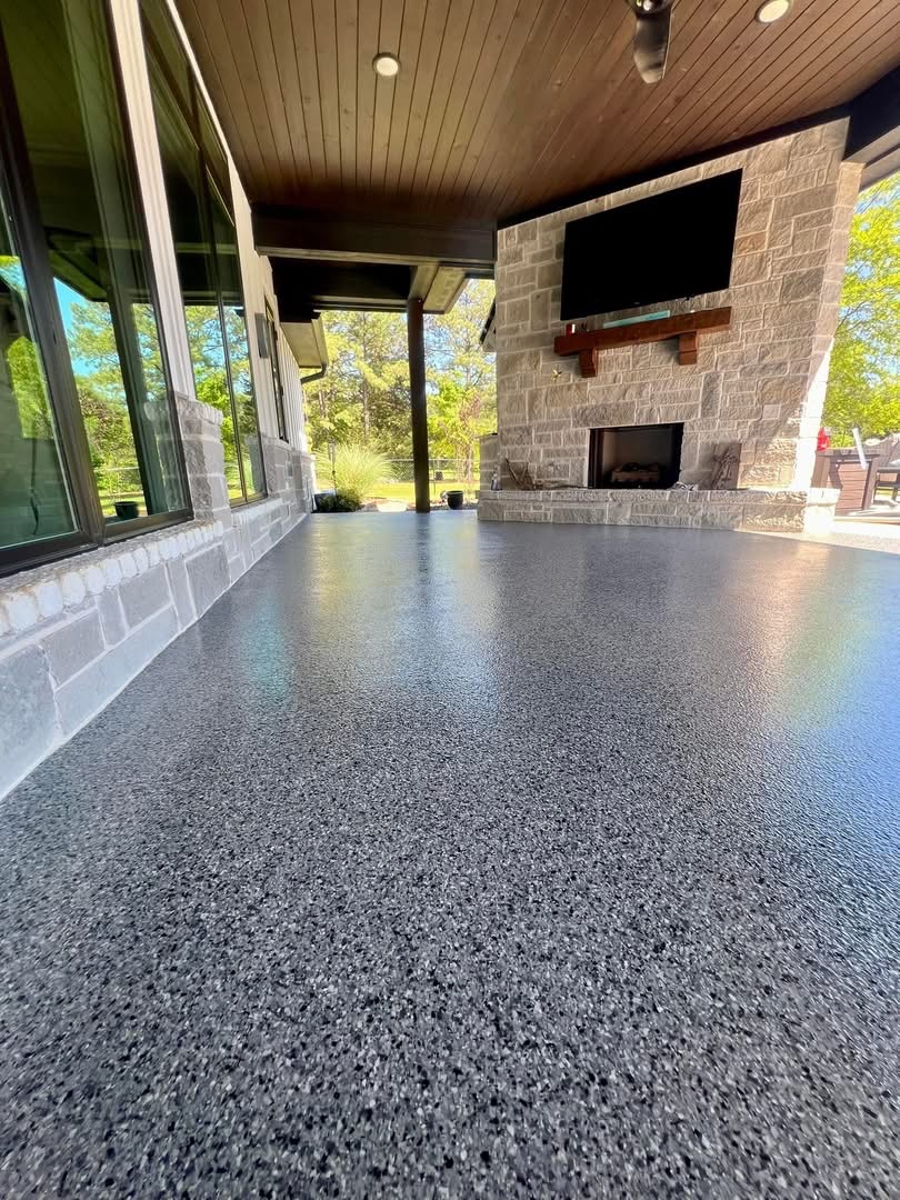 Covered patio with a stone fireplace and TV finished in a dark speckled flake floor coating