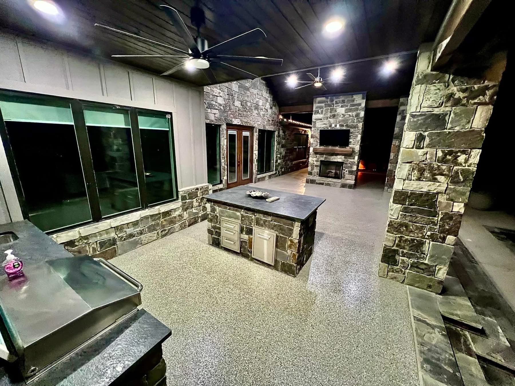 Covered outdoor living space with a stone fireplace finished in a speckled flake floor coating