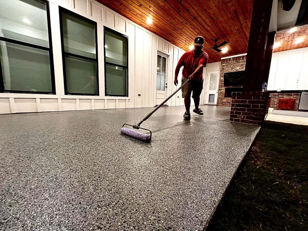 Crew member finishing a covered patio floor coating beside brick columns